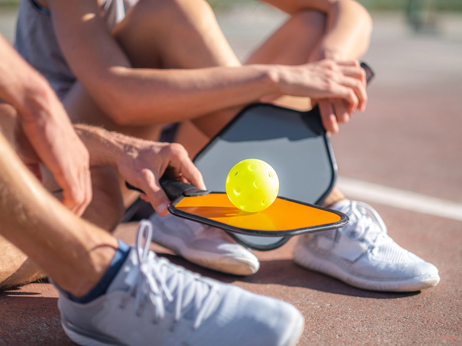 pickleball players sitting on ground with paddle and ball